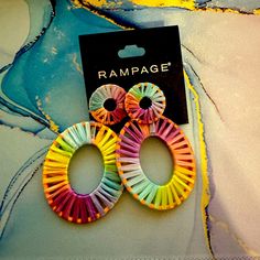 two pairs of multicolored paper earrings sitting on top of a blue and yellow cloth