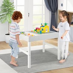 two young children playing with toys in a playroom area on the floor next to a white table