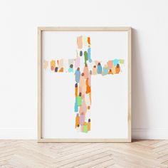 a cross made out of colorful dots on a white background in a wooden frame against a wall