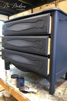 an image of a dresser being painted in dark blue and grey colors with paintbrushes on it