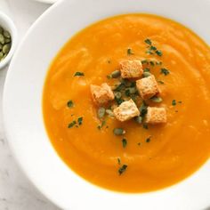 there is a bowl of carrot soup with croutons in it and two bowls next to it