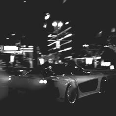 black and white photograph of a car driving down the street at night with blurry lights