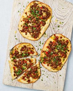 four pieces of bread with meat and herbs on it sitting on a cutting board next to a knife