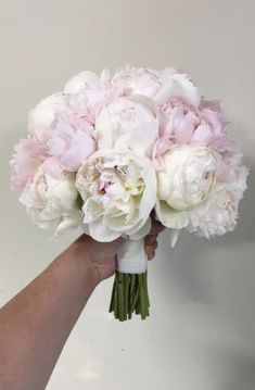 a hand holding a bouquet of white and pink peonies in front of a wall