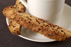 two pieces of bread on a white plate next to a cup of coffee and biscuits