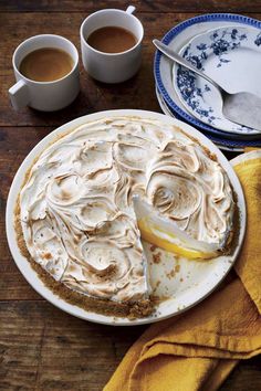 a pie on a plate next to two cups of coffee