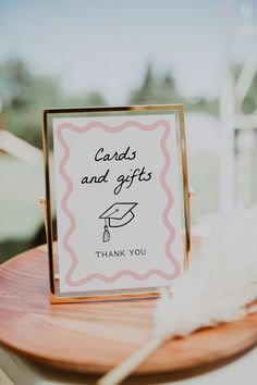 a card and gifts sign sitting on top of a wooden table next to a white feather