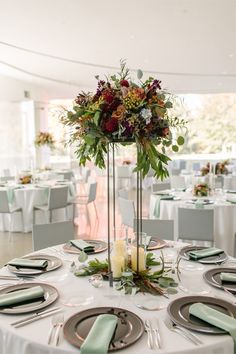 an elegant centerpiece with flowers and greenery is displayed on the table