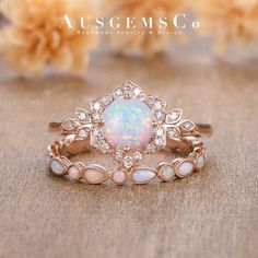 an opal and diamond ring set on top of a table with flowers in the background