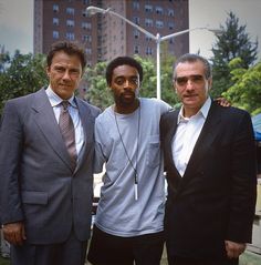 three men standing next to each other in front of a building with tall buildings behind them