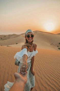 a woman holding the hand of a man on top of a sand dune at sunset