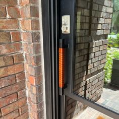 an orange door handle is on the outside of a brick building with a glass window