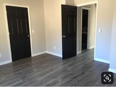 an empty room with black doors and wood flooring in the center is seen here