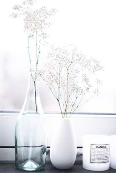 a vase with flowers in it sitting next to two candles on a window sill