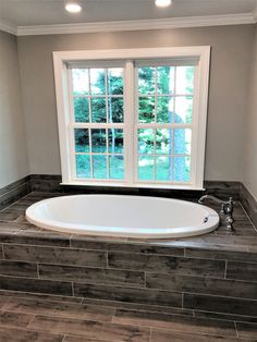 a large white bath tub sitting next to a window in a room with wood flooring