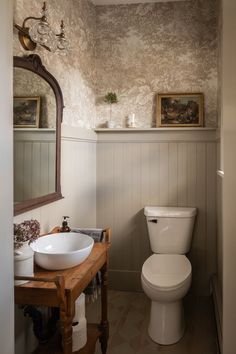 a white toilet sitting next to a bathroom sink under a mirror on top of a wooden table