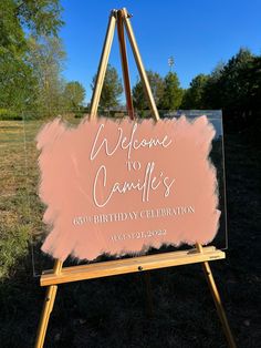 a welcome sign is displayed on an easel in front of some grass and trees