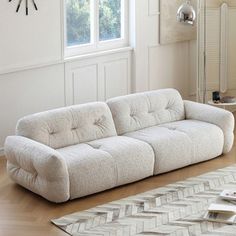 a white couch sitting on top of a hard wood floor next to a clock mounted on the wall