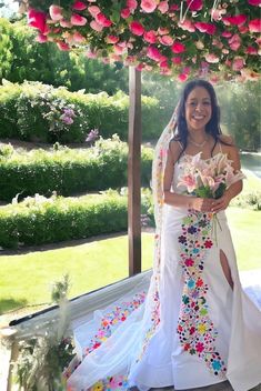 a woman in a wedding dress standing under a flower covered structure