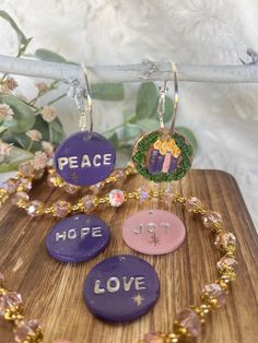 peace, hope, and love charms are displayed on a wooden board with flowers in the background