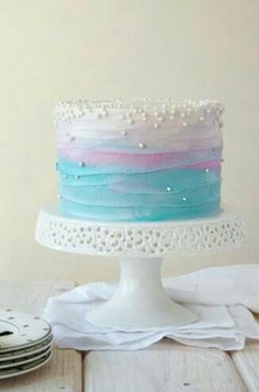 a multi - colored cake sitting on top of a white cake stand next to plates