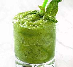 a green smoothie in a glass with a straw and mint garnish on top