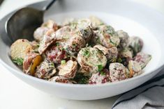 a white bowl filled with potato salad on top of a table next to a spoon