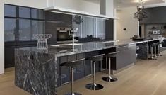 a large kitchen with marble counter tops and stainless steel appliances, along with bar stools