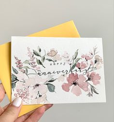 a person holding up a card with flowers on it and the words happy anniversary written in cursive writing