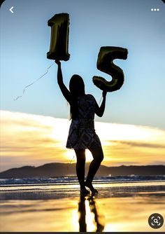 a girl holding up the number five balloon in front of her face at the beach