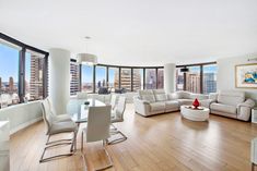 a living room filled with white furniture and large windows overlooking the cityscape in the distance