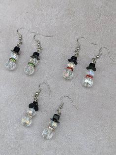 six pairs of snowman earrings with black bows and crystal beads on white carpeted surface