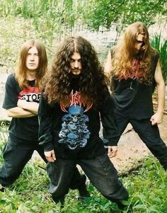 three men with long hair standing in the grass