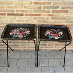 two black trays with flowers painted on them are sitting next to a brick wall