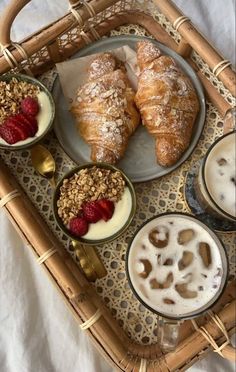 a wicker tray topped with croissants and bowls of food next to drinks