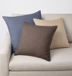 three pillows sitting on top of a couch in front of a white wall with a black and brown checkerboard pattern