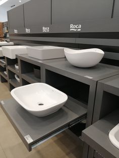 a row of sinks in a bathroom with gray counter tops and white bowls on them