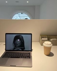 an open laptop computer sitting on top of a white desk next to a cup of coffee