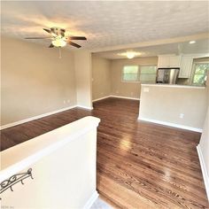 an empty living room with hard wood flooring and ceiling fan in the center area