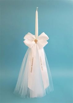 a white candle with a ribbon around it on a blue background in the shape of a bow