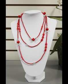 a red beaded necklace on a white mannequin with flowers in the background