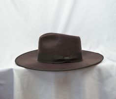 This dark brown soft high quality brushed felt flat brim 4-inch fedora with pinched fedora crown has a 1 1/2 inch grosgrain ribbon with a bow around the crown and an elastic tie in the crown which will fit up to a 57CM (22 5/8 inch) head size. Brown Brimmed Felt Hat For Formal Occasions, Brown Fedora Felt Hat For Formal Occasions, Formal Brown Fedora Felt Hat, Brown Formal Fedora Hat, Formal Brown Fedora Hat, Brown Wide Brim Fedora For Formal Occasions, Brown Formal Fedora With Curved Brim, Formal Brown Fedora With Curved Brim, Vintage Solid Color Felt Hat With Flat Brim