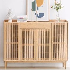 a wooden cabinet sitting next to a vase with flowers in it and a painting on the wall