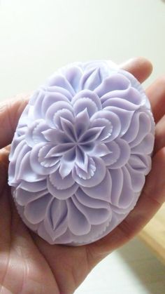 a hand holding a purple flower in it's right hand and another object in the background