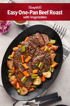 a black plate topped with meat and veggies on top of a white table