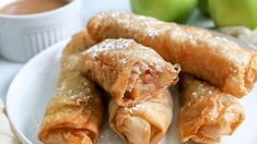 some food is on a white plate and has powdered sugar on the top, and green apples in the background