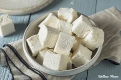 a bowl filled with white marshmallows on top of a blue wooden table