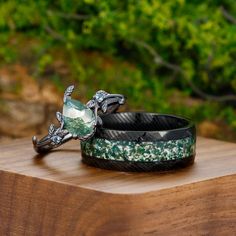 two bracelets sitting on top of a wooden table in front of some green trees