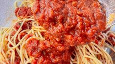 spaghetti and sauce being mixed together in a glass bowl with a metal spoon on the side