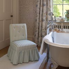 a bath tub sitting next to a white chair in a room with floral wallpaper